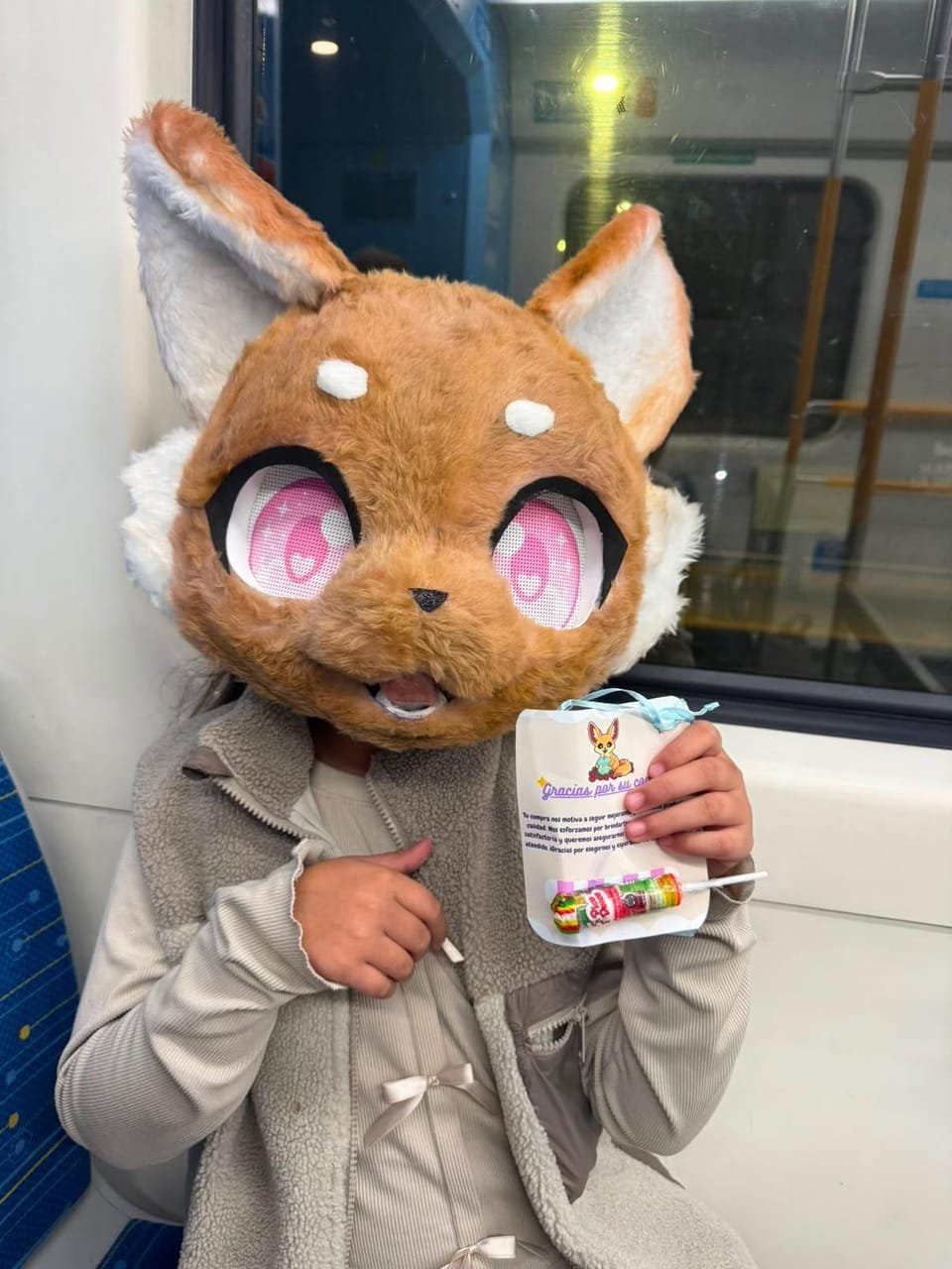 Clienta con su cabeza de fursuit naranja puesta, sosteniendo una tarjeta de agradecimiento.